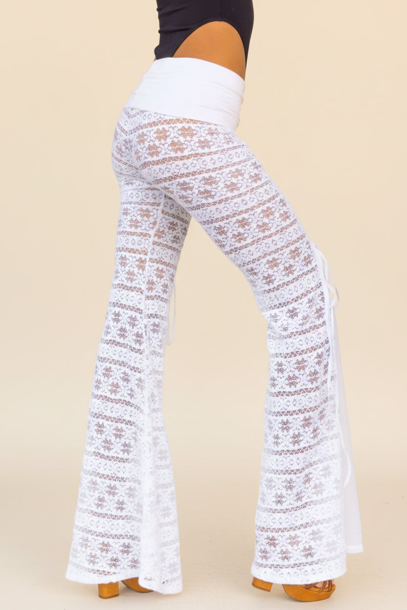 White crochet lace flare pants with side tie details, shown on a model from the side.