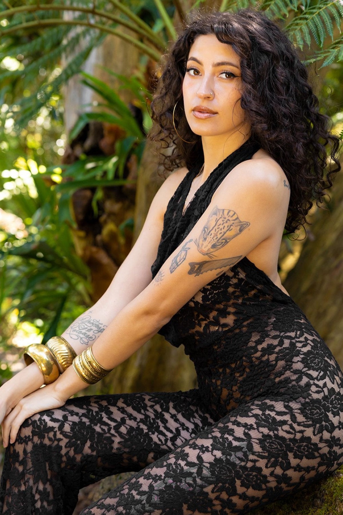 Woman wearing a black lace outfit with tattoos sitting in a natural setting