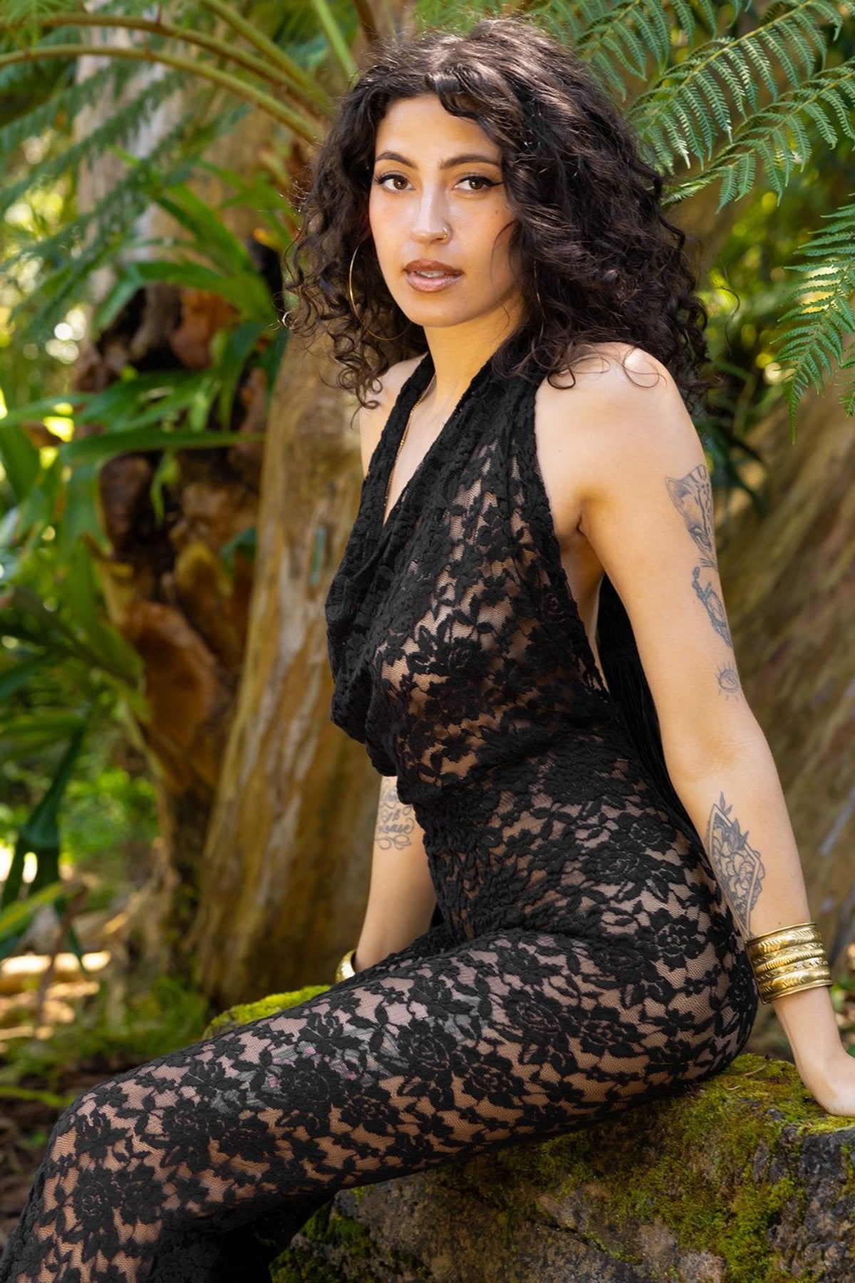 Woman wearing a black lace outfit sitting in a natural setting with greenery.