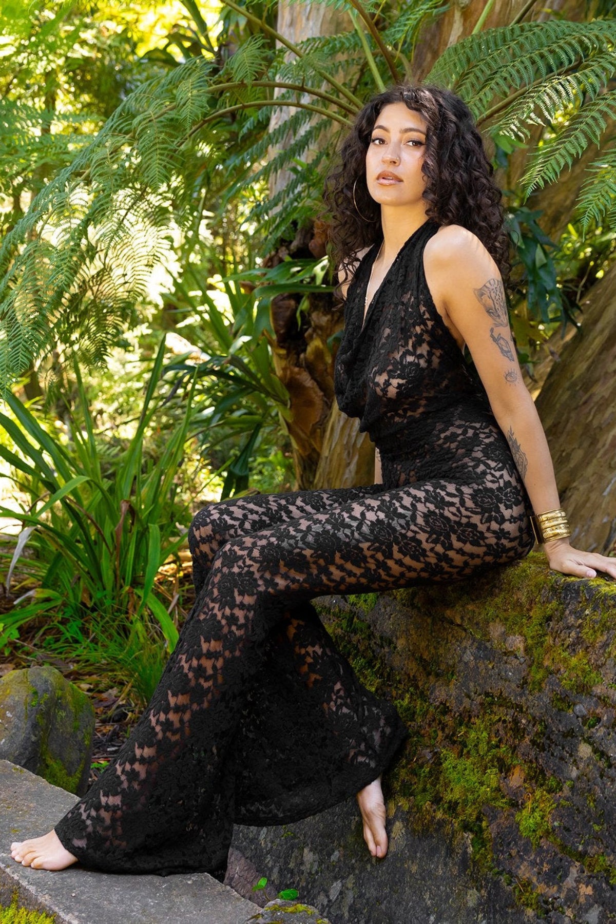 Woman in a black lace outfit sitting on a rock in a garden setting