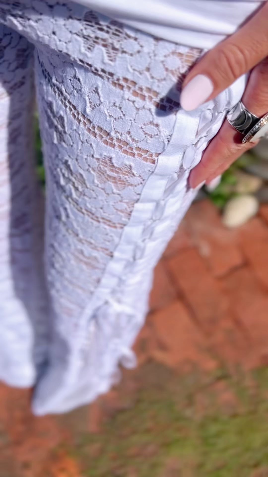 A close up shot of white crochet lace pants with a corset detail, white mesh, and velvet ribbon.